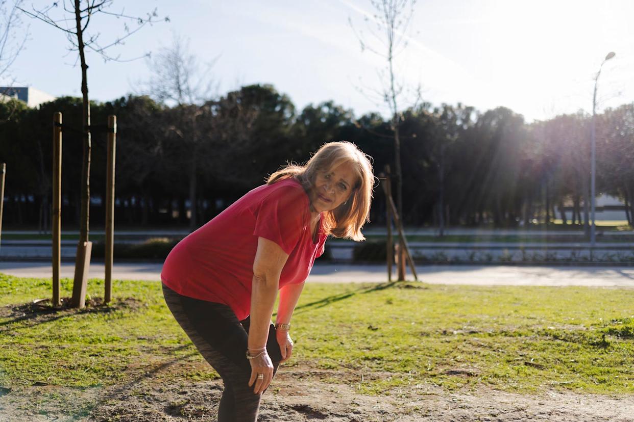 An elderly woman in a red shirt feels short of breath and has to pause her training