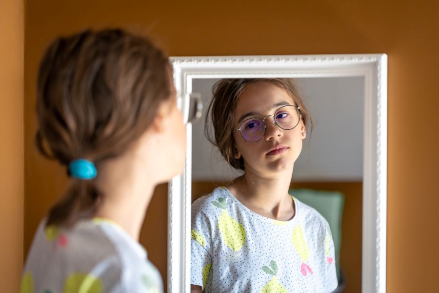 A young girl looks unhappily in the mirror