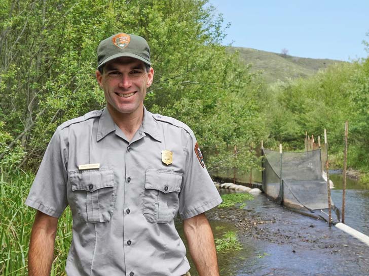 National park researcher Michael Reichmuth stands in front of a wooded area.