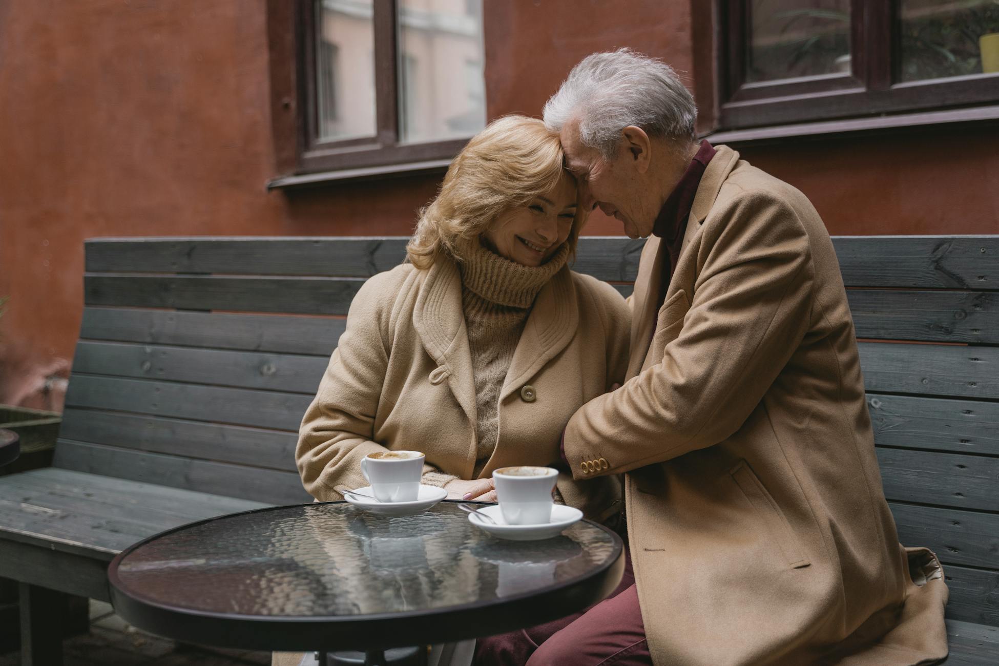 Lovely elderly couple sharing coffee on a cozy outdoor bench and expressing warmth and affection.