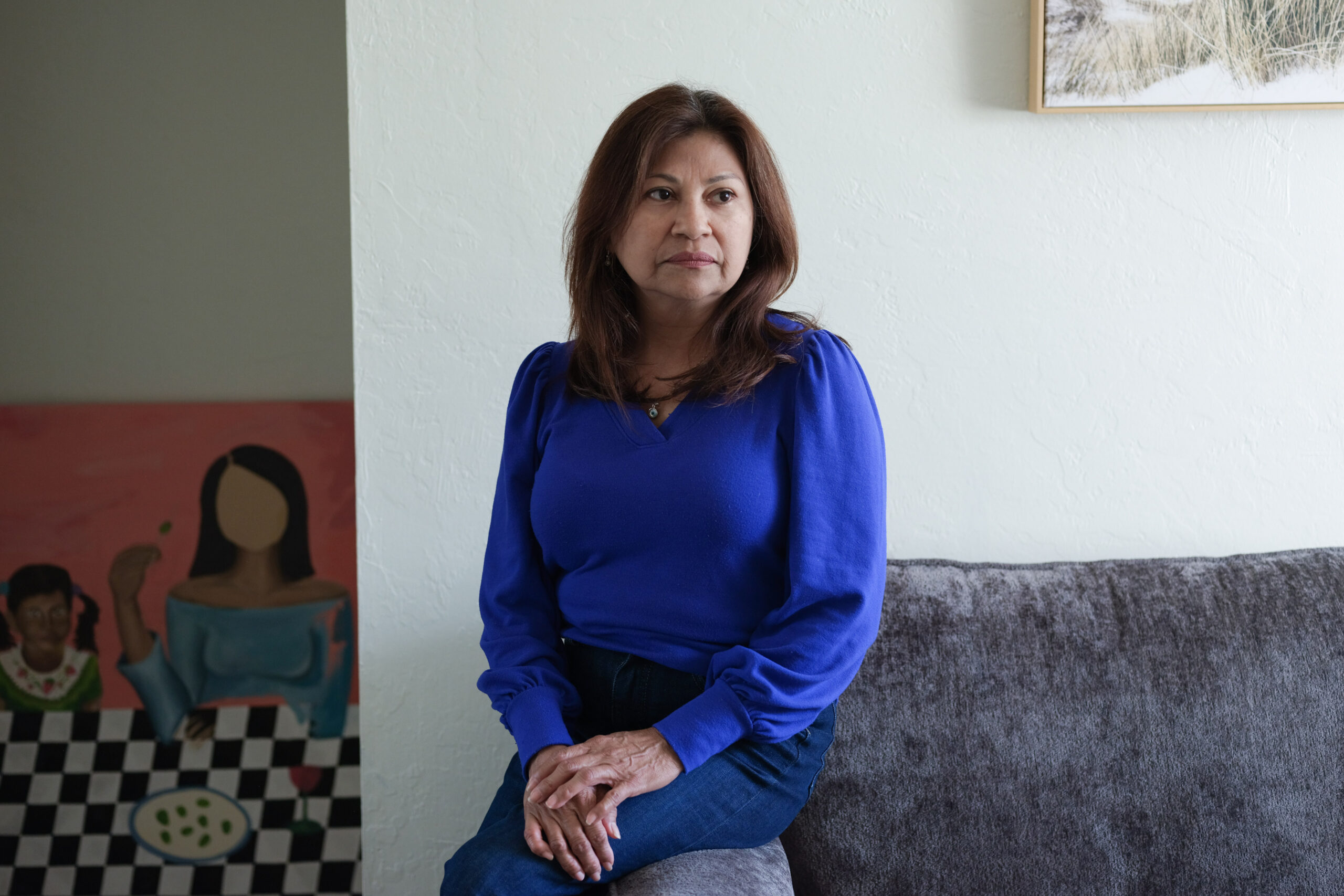 Lorena Alvarado Hill is sitting on the edge of the couch. A mural can be seen on the wall behind her.
